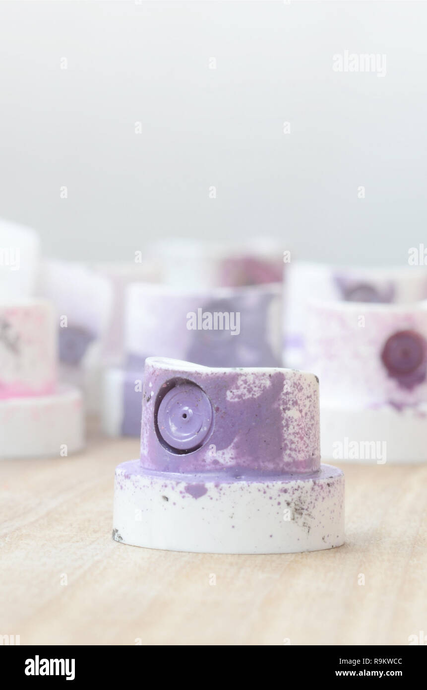 Several plastic nozzles from a paint sprayer that lie on a wooden surface against a gray wall background. The caps are smeared in violet paint. The co Stock Photo