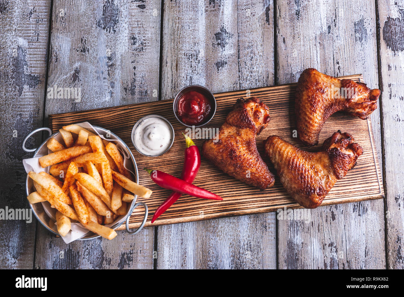 Grilled chicken wings, french fries, white and red sauce nuts on a wooden surface Stock Photo