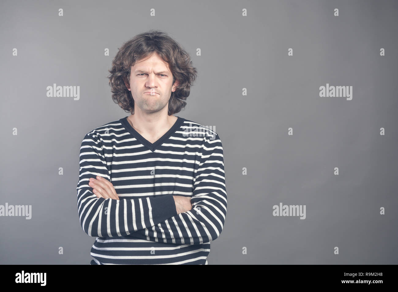 Closeup portrait of displeased, angry, grumpy man in striped sweater bad attitude, arms crossed, folded, looking at you, isolated gray background. Neg Stock Photo