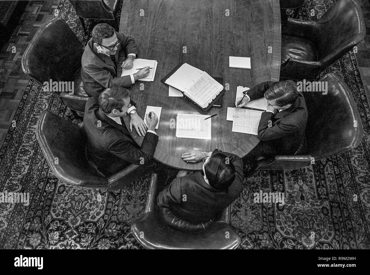 At a conference table on an oriental carpet, four life insurance company executives compare information charts in Boston, MA. Stock Photo