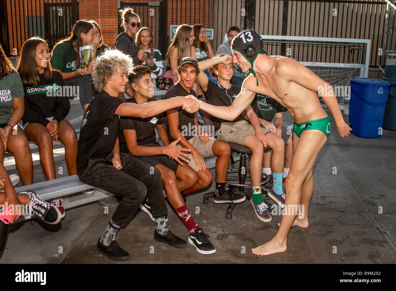 Multiracial high school water polo team members in robes and numbered caps shake hands with welcoming student admirers before a game in Costa Mesa, CA. Stock Photo