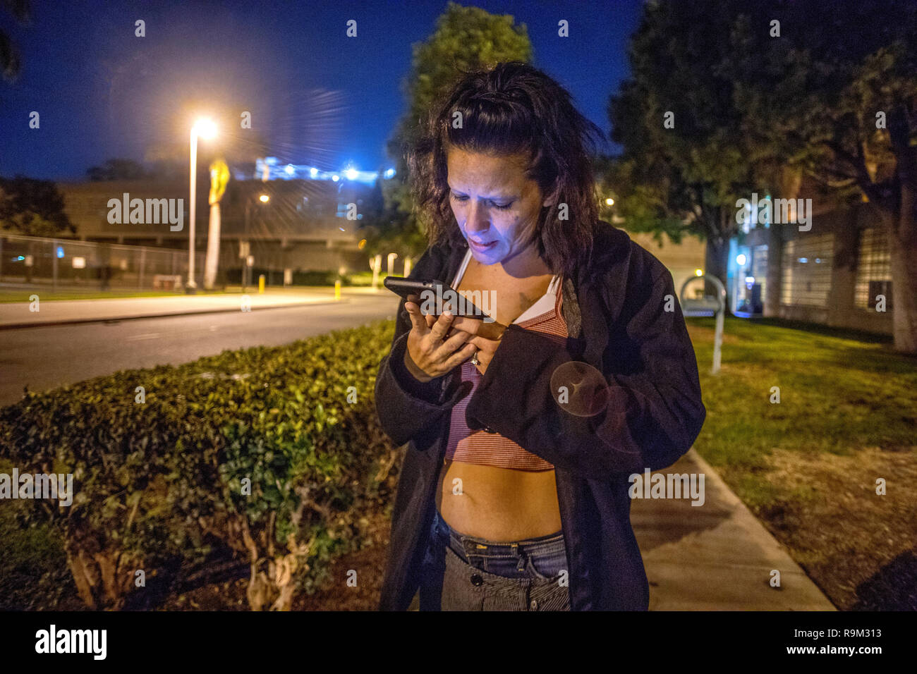 An released county jail inmate uses a donated charity cell phone to call for a ride at night in Santa Ana, CA. Stock Photo