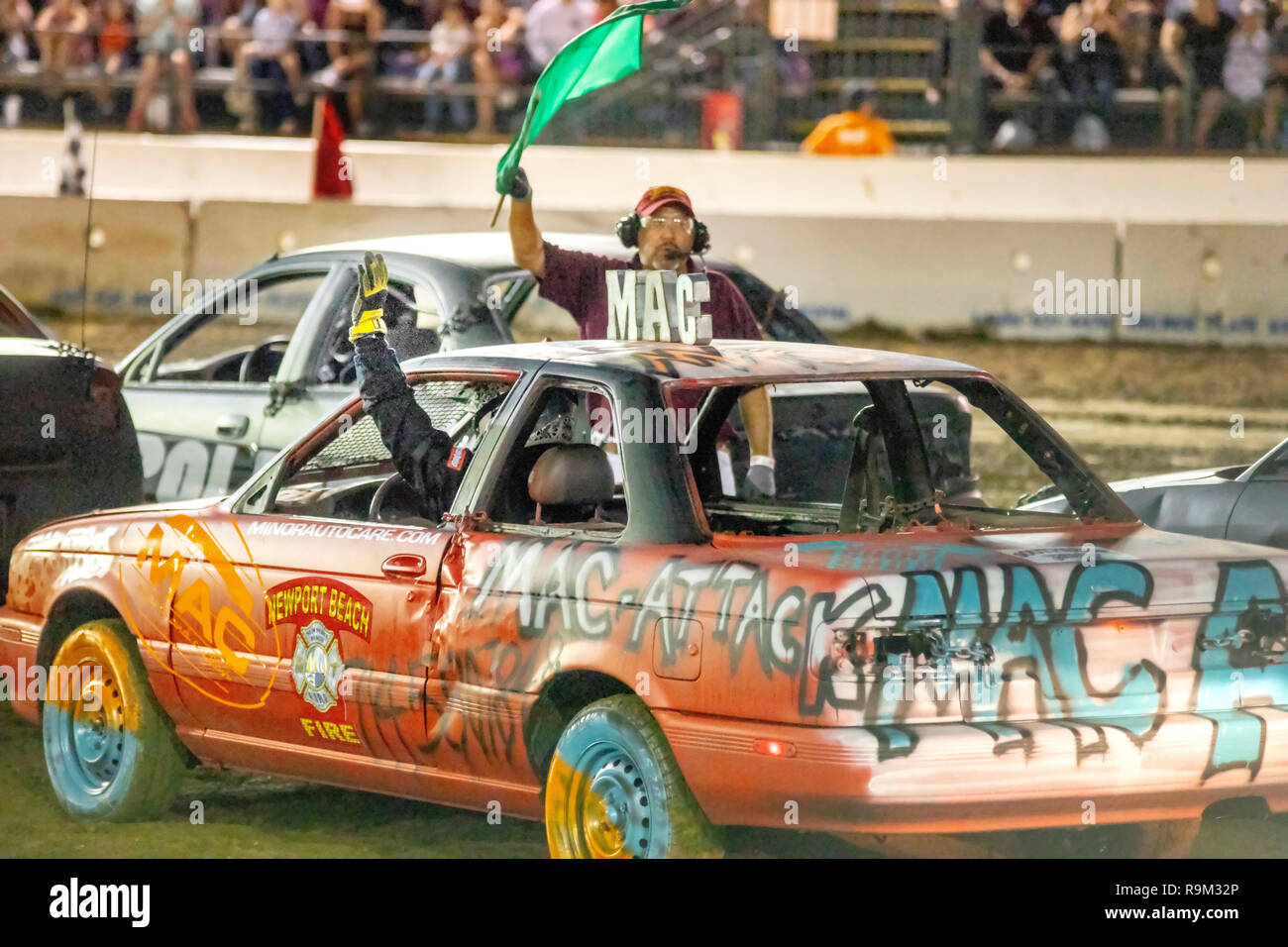 A referee waves a green flag to signal the start of a car-crashing demo derby in a Costa Mesa, CA, stadium. Stock Photo