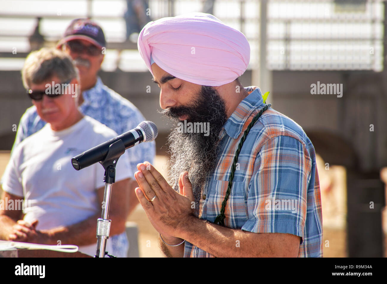 In beard and turban, a Sikh community speaker offers a prayer at an outdoor interfaith observance in Huntington Beach, CA. Stock Photo