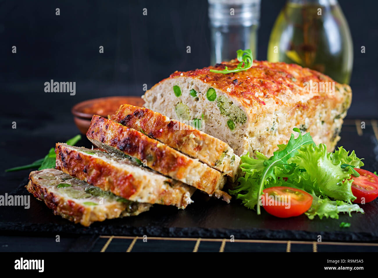 Tasty homemade ground  baked chicken meatloaf with green peas and broccoli on black table. Food american meat loaf. Stock Photo