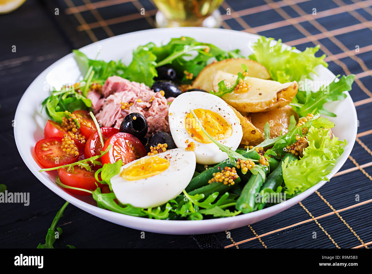 Healthy hearty salad of tuna, green beans, tomatoes, eggs, potatoes, black olives close-up in a bowl on the table. Salad Nicoise. French cuisine. Stock Photo