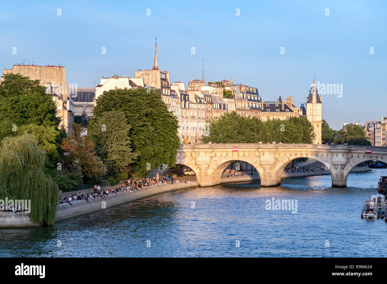 Cite island and Pont Neuf in Paris on a sunny summer. People are sitting on the river bank. Stock Photo