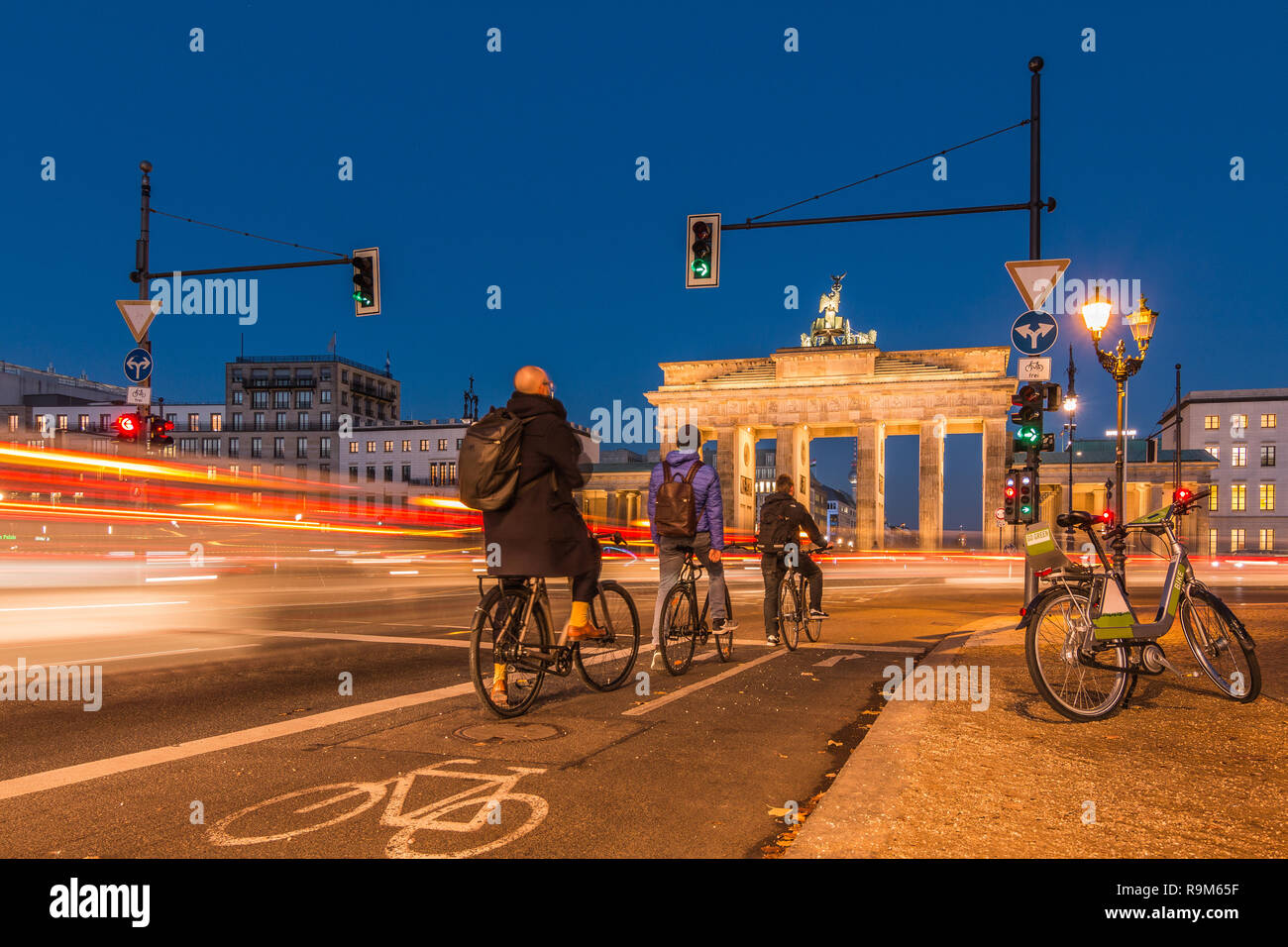 Backside of the Brandenburg Gate at night. Cyclists are waiting at the traffic light. passing cars in long-term exposure. An e-bike is on the roadside Stock Photo