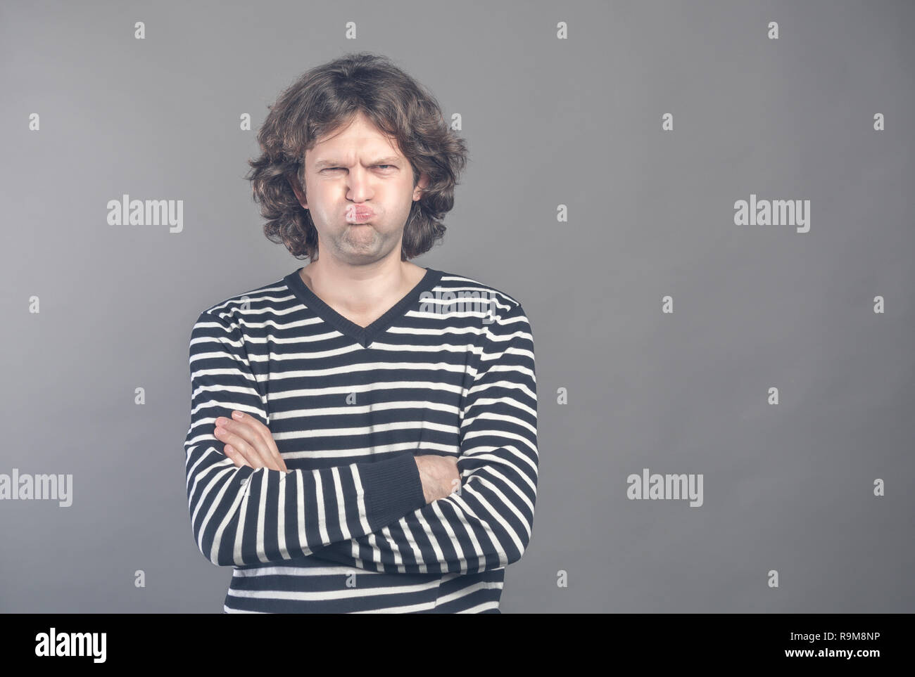 Funny comic man pouts lips and cheeks makes angry grimace, foolishes after all day working. Clueless male nerd with awkward expression has fun alone,  Stock Photo