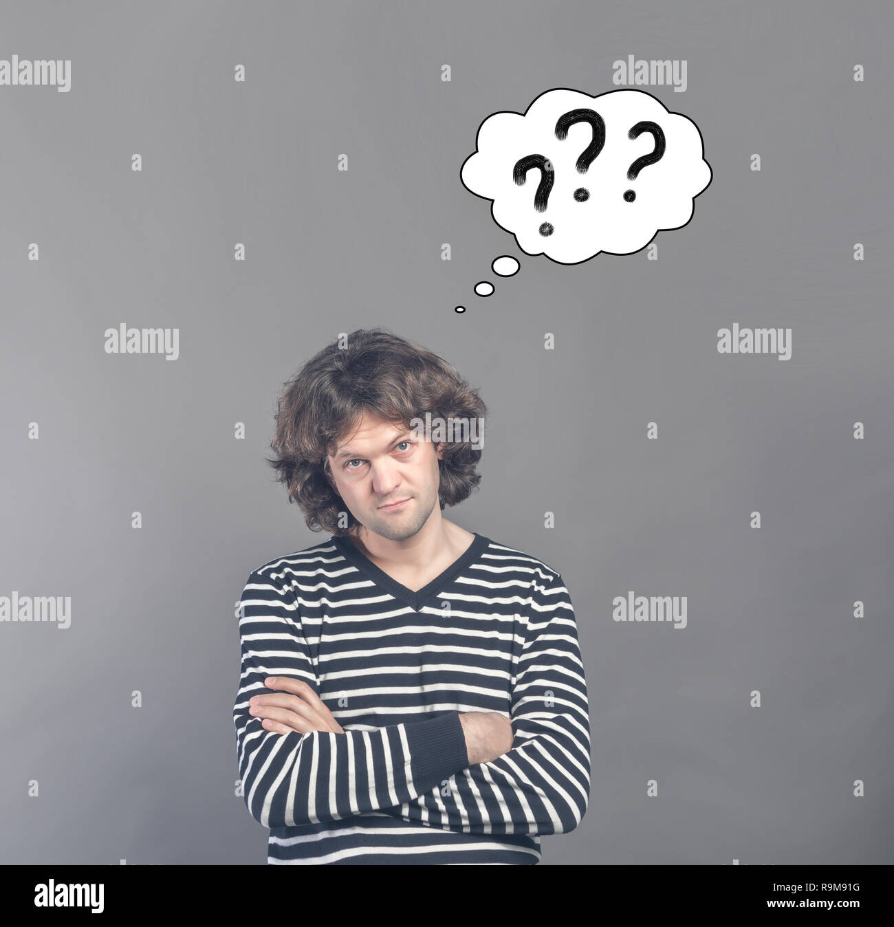 Skeptical man looking suspicious and questionable with drawn cloud of thoughts with three question marks in it. Some disapproval on face on gray backg Stock Photo