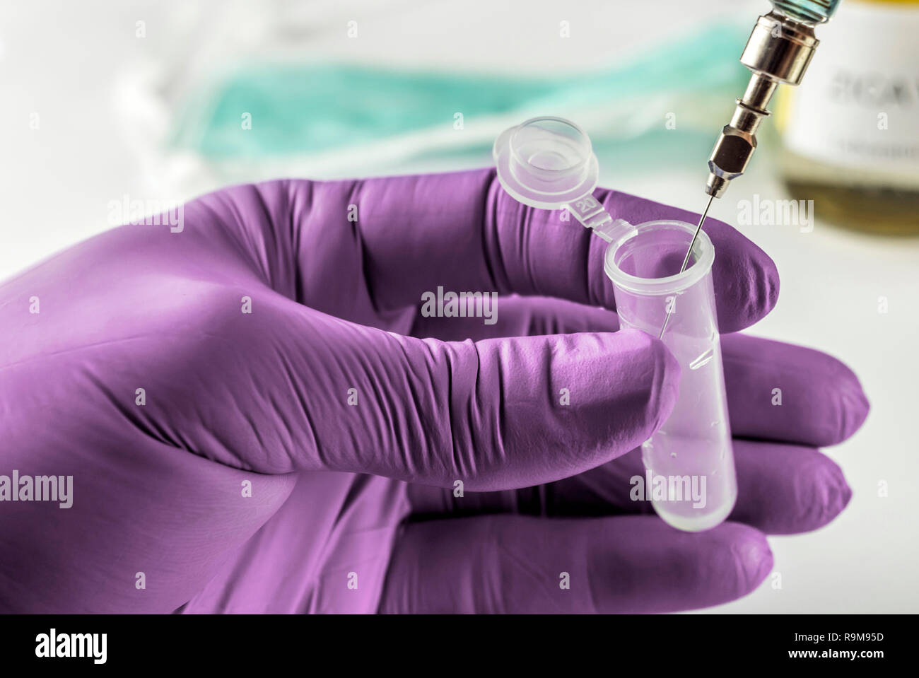 Scientist with green latex gloves manipulates vial and syringe in laboratory, conceptual image Stock Photo