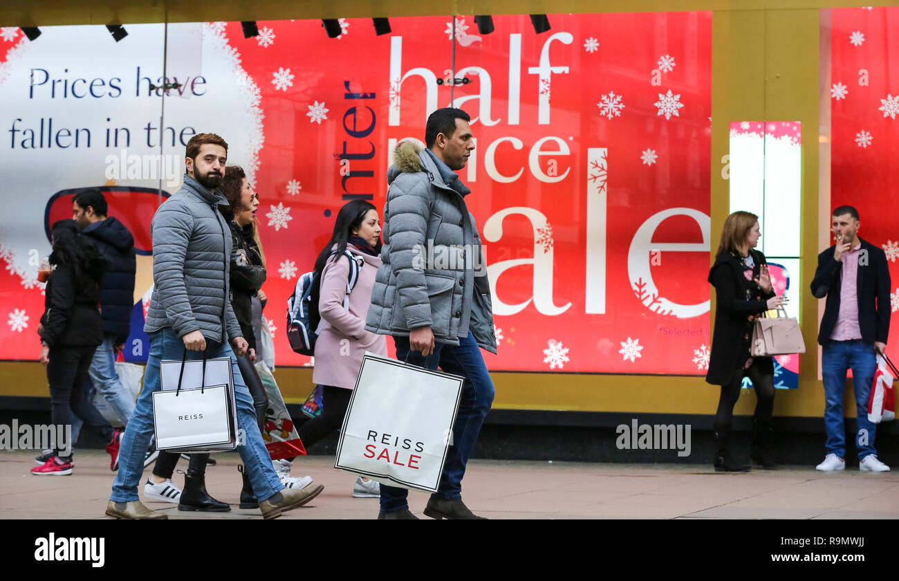 Shoppers are seen with shopping bags walking past a Winter Half Price Sale window display on London s Oxford Street. Tens of thousands of shoppers are seen taking advantage of post Christmas bargains ...