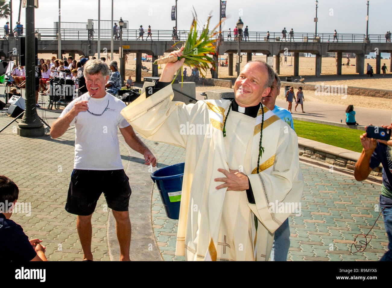Waving a palm frond, a priest in vestments sprinkles holy water on a