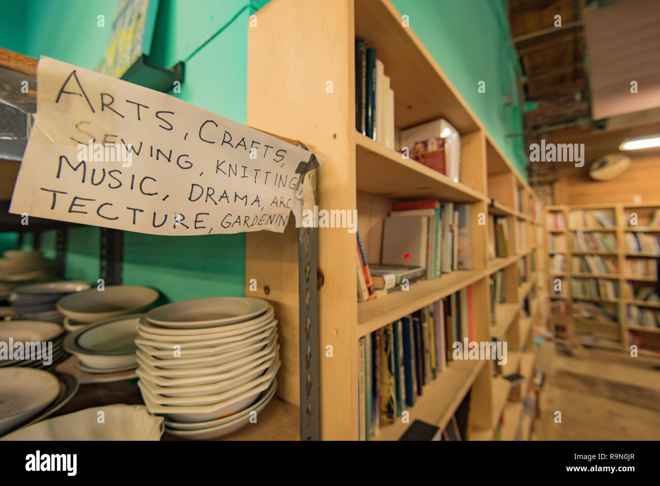 A hand written sign above books and crockery (plates) stacked on shelves in a Thrift Store in the Mission district of San Francisco, California, USA Stock Photo