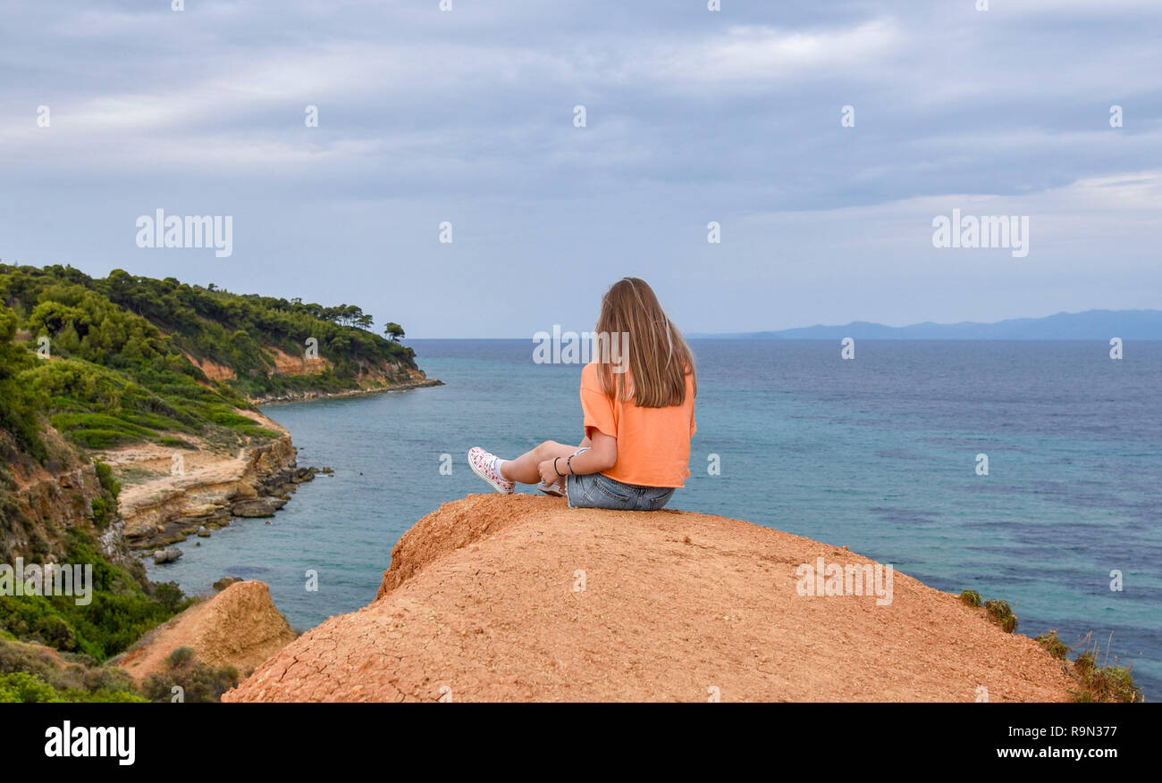 Girl sitting on a cliff above the sea Stock Photo Alamy