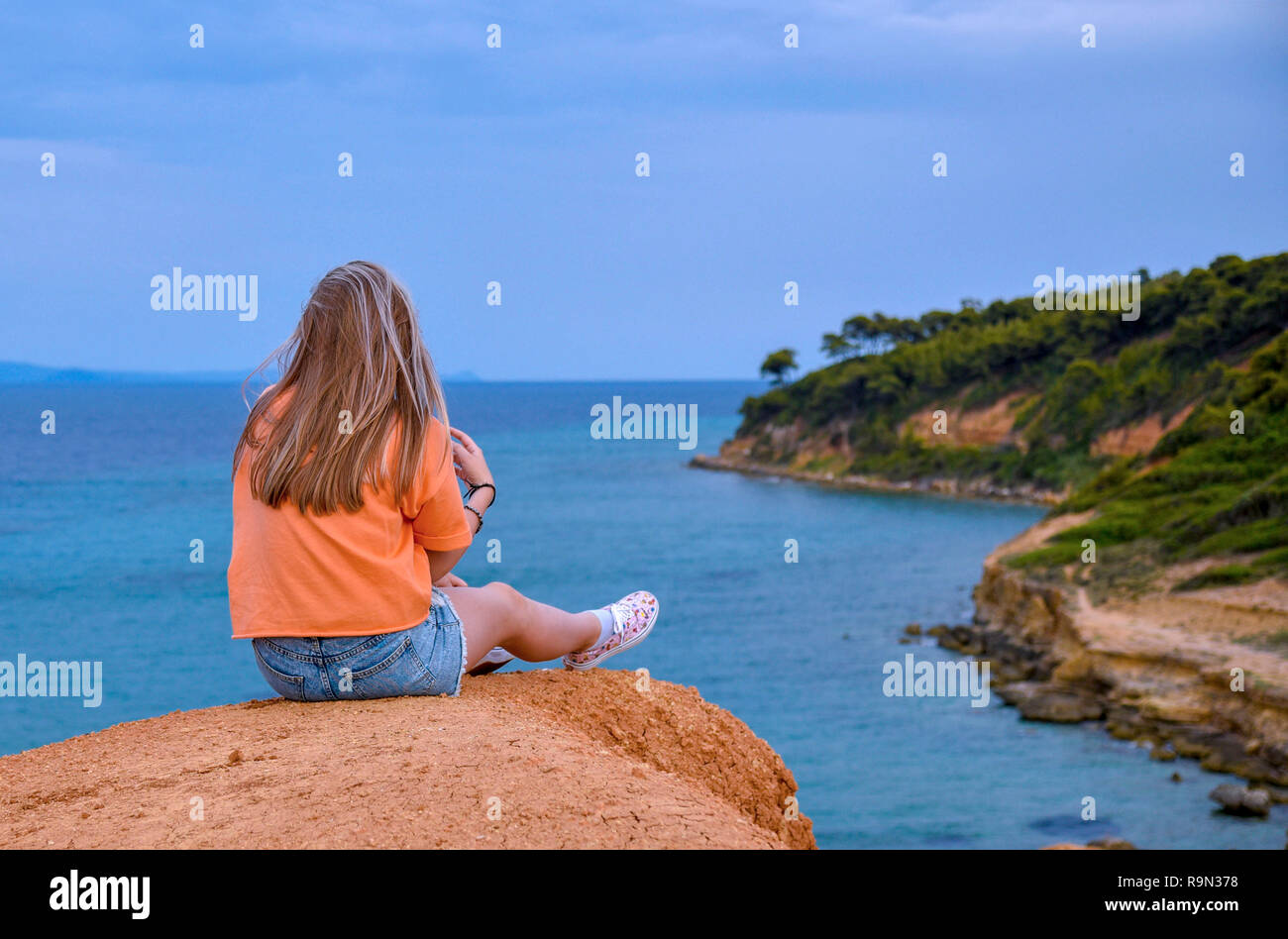 Girl sitting on a cliff above the sea Stock Photo - Alamy