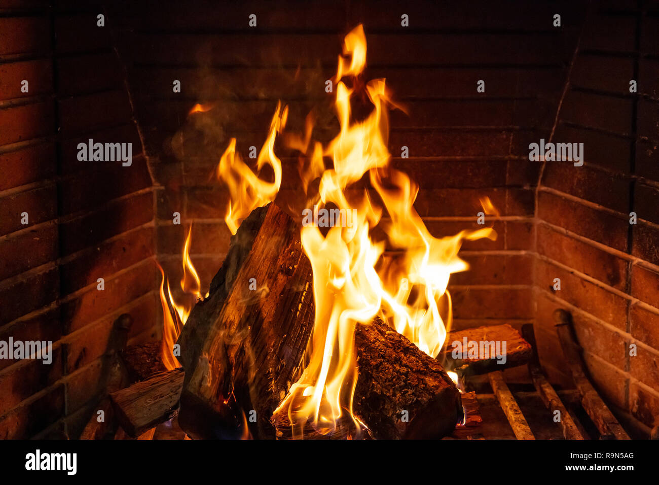 Christmas time, cozy fireplace. Wood logs burning against red firebricks  background, relaxation and warm home Stock Photo - Alamy