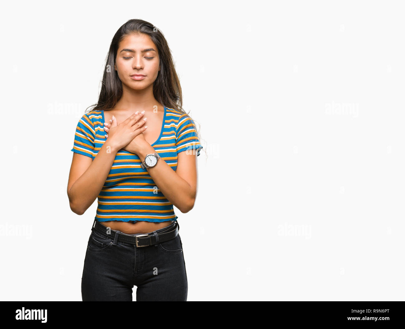 Young beautiful arab woman over isolated background smiling with hands on chest with closed eyes and grateful gesture on face. Health concept. Stock Photo
