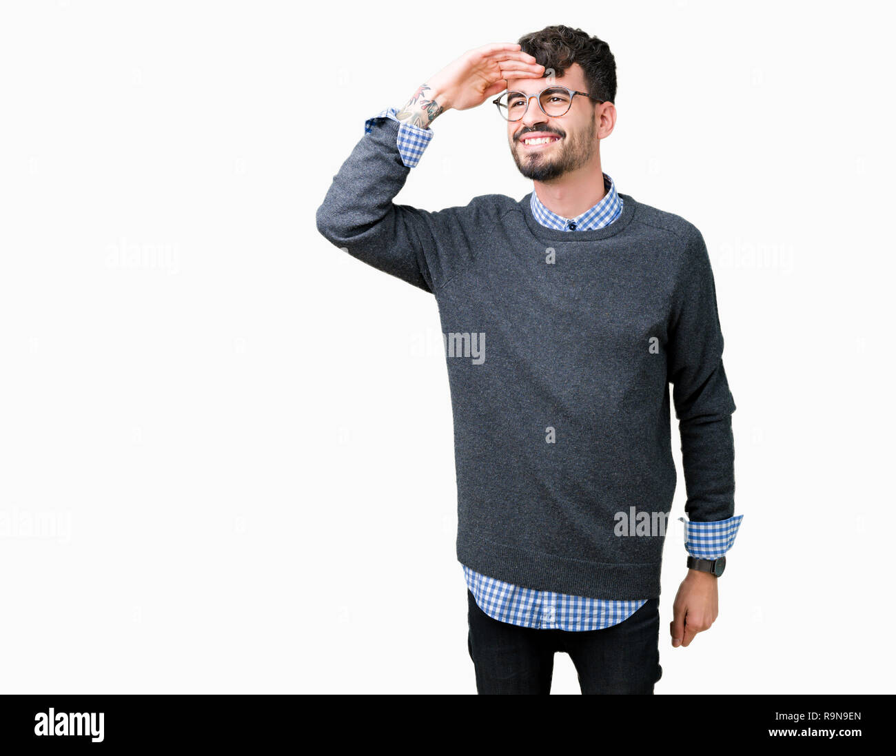 Young handsome smart man wearing glasses over isolated background very happy and smiling looking far away with hand over head. Searching concept. Stock Photo