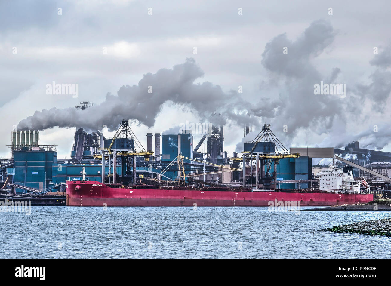 IJmuiden, The Netherlands, December 22, 2018: smoking chimneys and a red bulk carrier moored at the Tata steelworks on the opposite side of the Norths Stock Photo