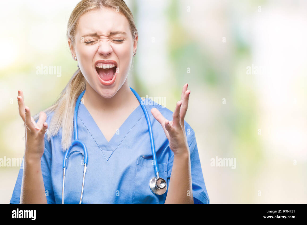 Young blonde surgeon doctor woman over isolated background crazy and mad shouting and yelling with aggressive expression and arms raised. Frustration  Stock Photo