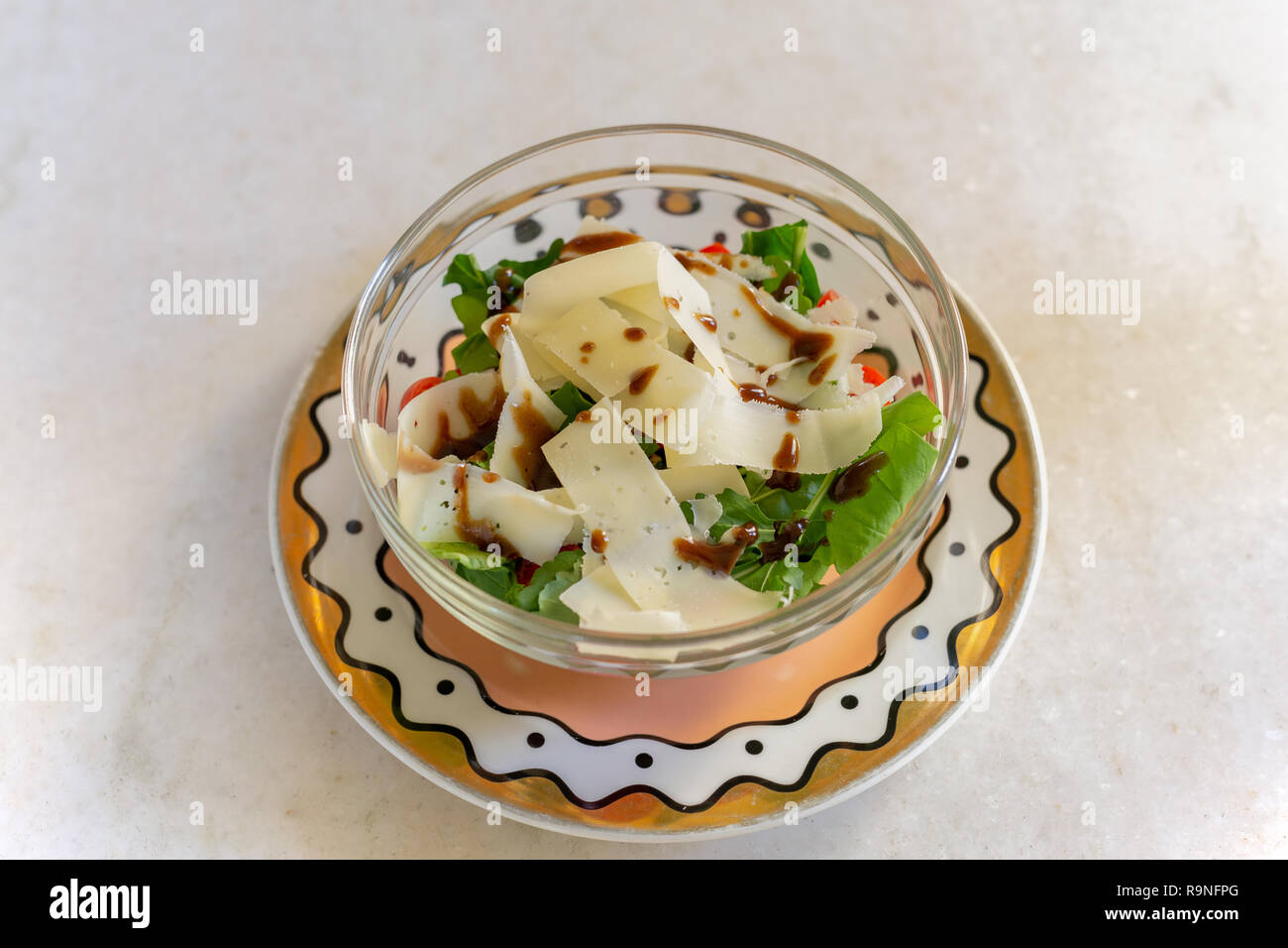 Green vegetable salad with slice of parmesan cheese in glass bowl. Stock Photo