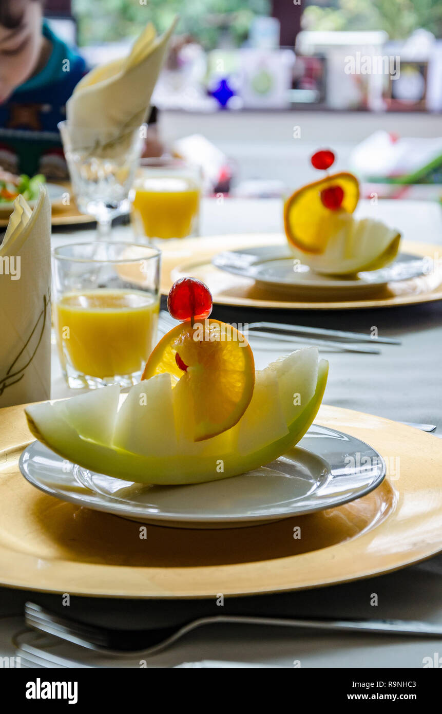 A slice of melon presented as a melon boat on a plate on a dining room table ready to eat as a first course. Stock Photo