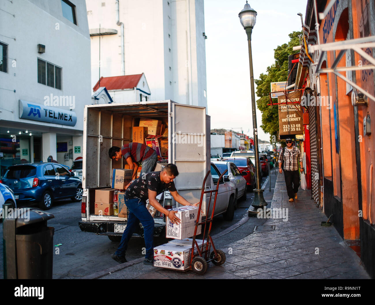 Two young workers in parcels unload several packages of a transport truck. Daily life in the historic center of Hermosillo, Sonora, Mexico. Telmex Bui Stock Photo