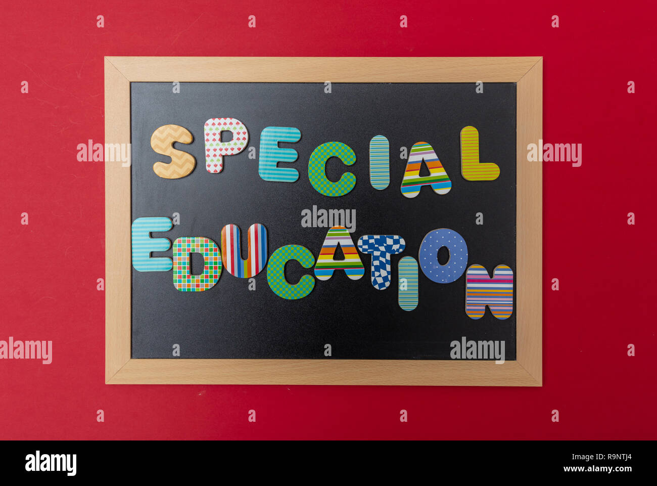 Special education concept. Black chalkboard with wooden frame, text special education in colorful letters, red wall background Stock Photo