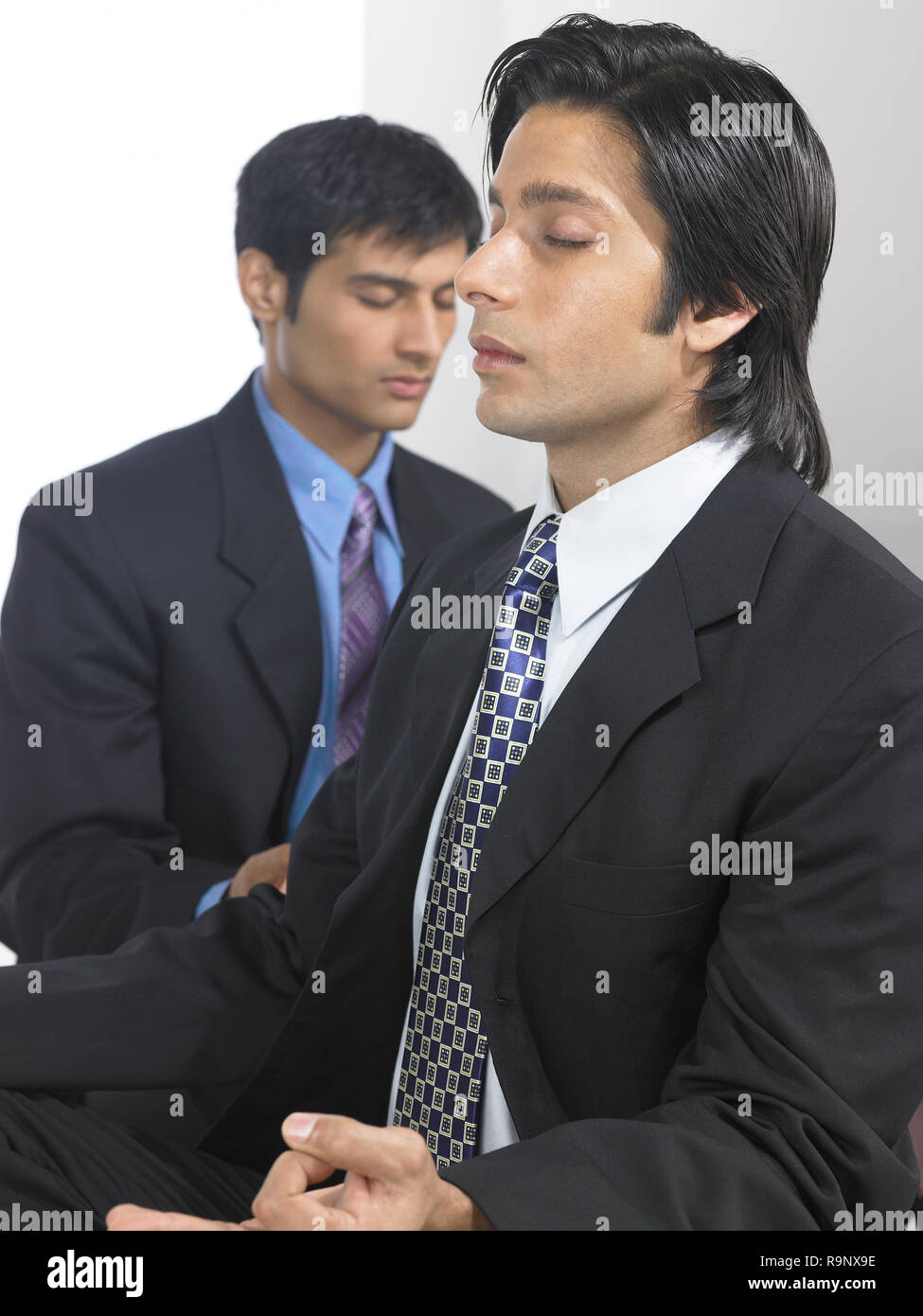 PORTRAIT OF TWO CORPORATE EXECUTIVES MEDITATING AGAINST A WHITE
