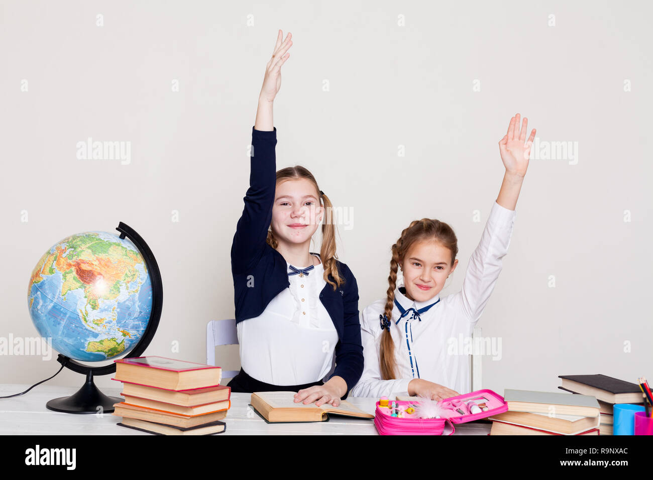 two schoolgirls girls in class at her desk with books hand to answer ...