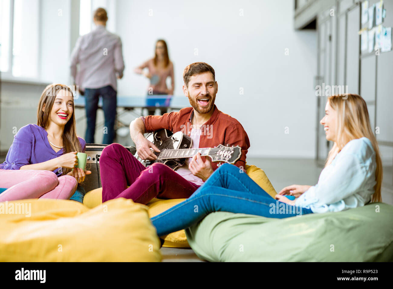 Group of a young coworkers having fun playing guitar and playing small  tennis during the coffee break in the office Stock Photo - Alamy