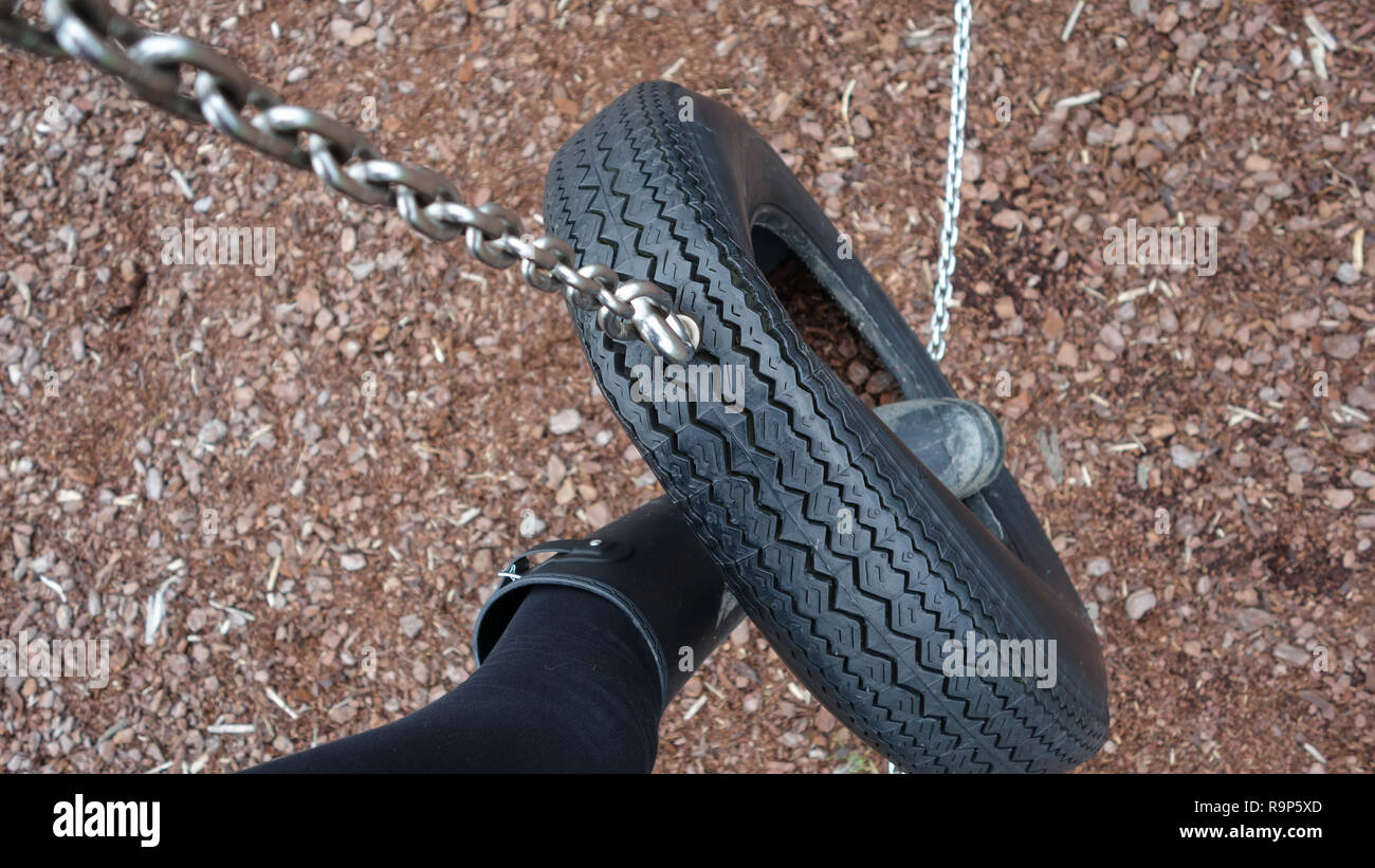 Black welly boot in a tyre swing above wood chip Stock Photo