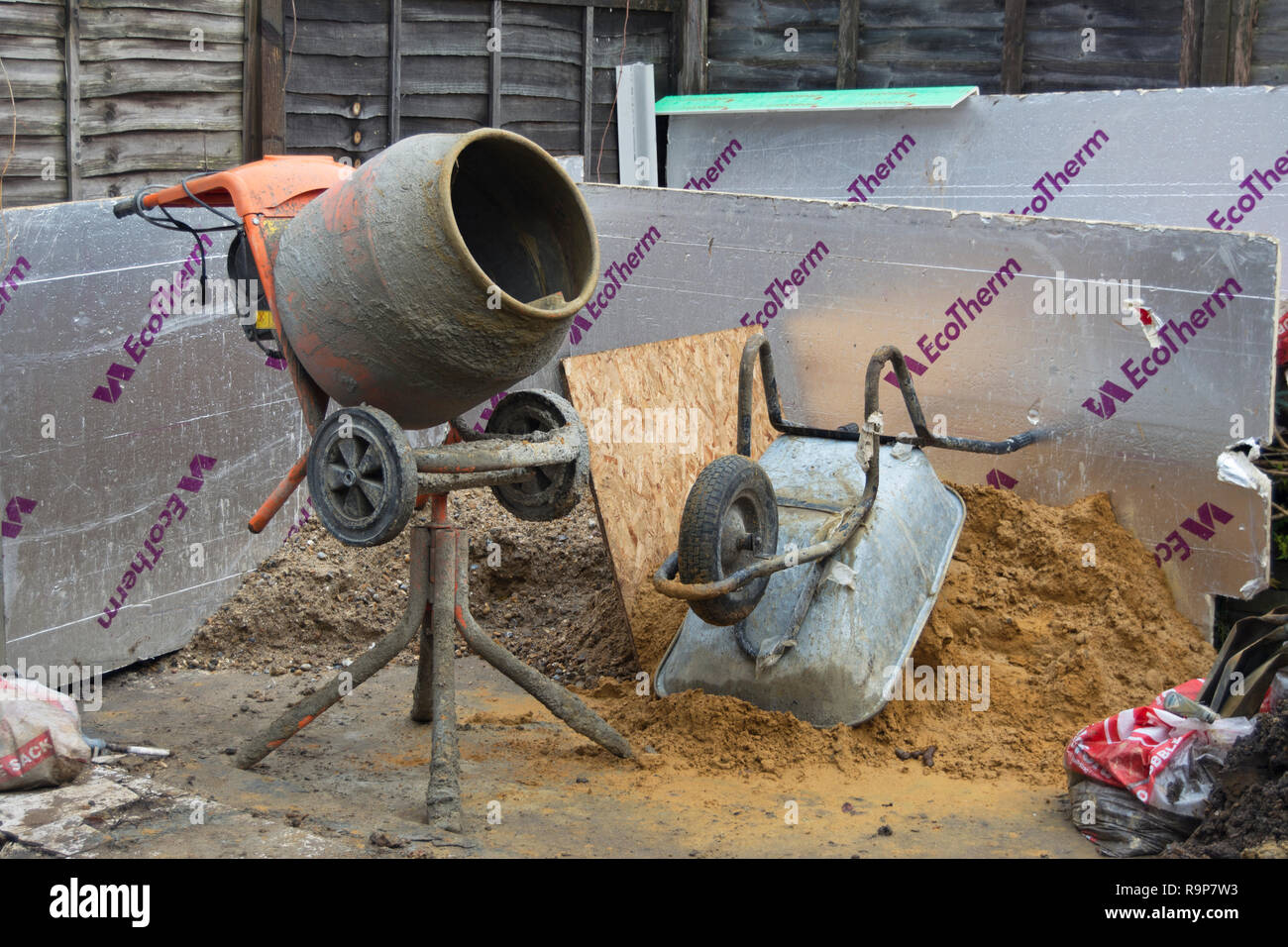 cement mixer and upturned wheelbarrow beside a pile of sand and rubble, and insulation panels, at a house refurbishment in twickenham, england Stock Photo