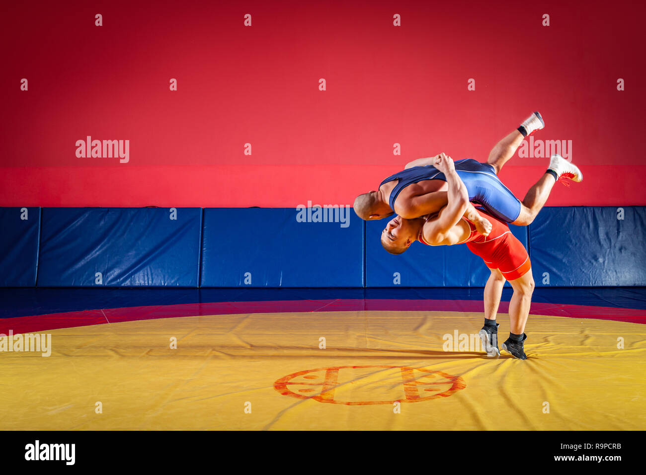 Two young men in blue and red wrestling tights are wrestlng and making a  suplex wrestling on a yellow wrestling carpet in the gym. The concept of  fair Stock Photo - Alamy