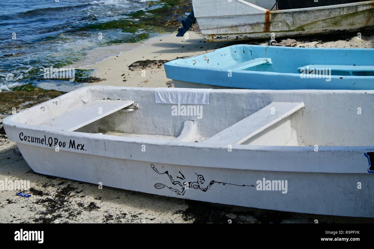 Boats on a Caribbean islands rock shoreline pulled up onto the white sand beach Stock Photo