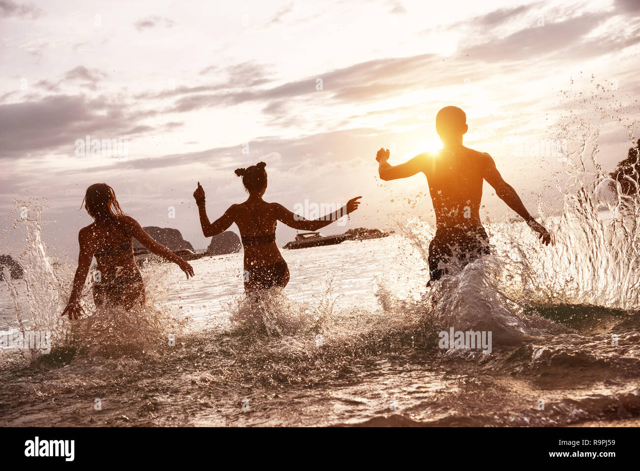 Group of happy friends run and jump at sunset sea beach. Tropical vacations concept Stock Photo