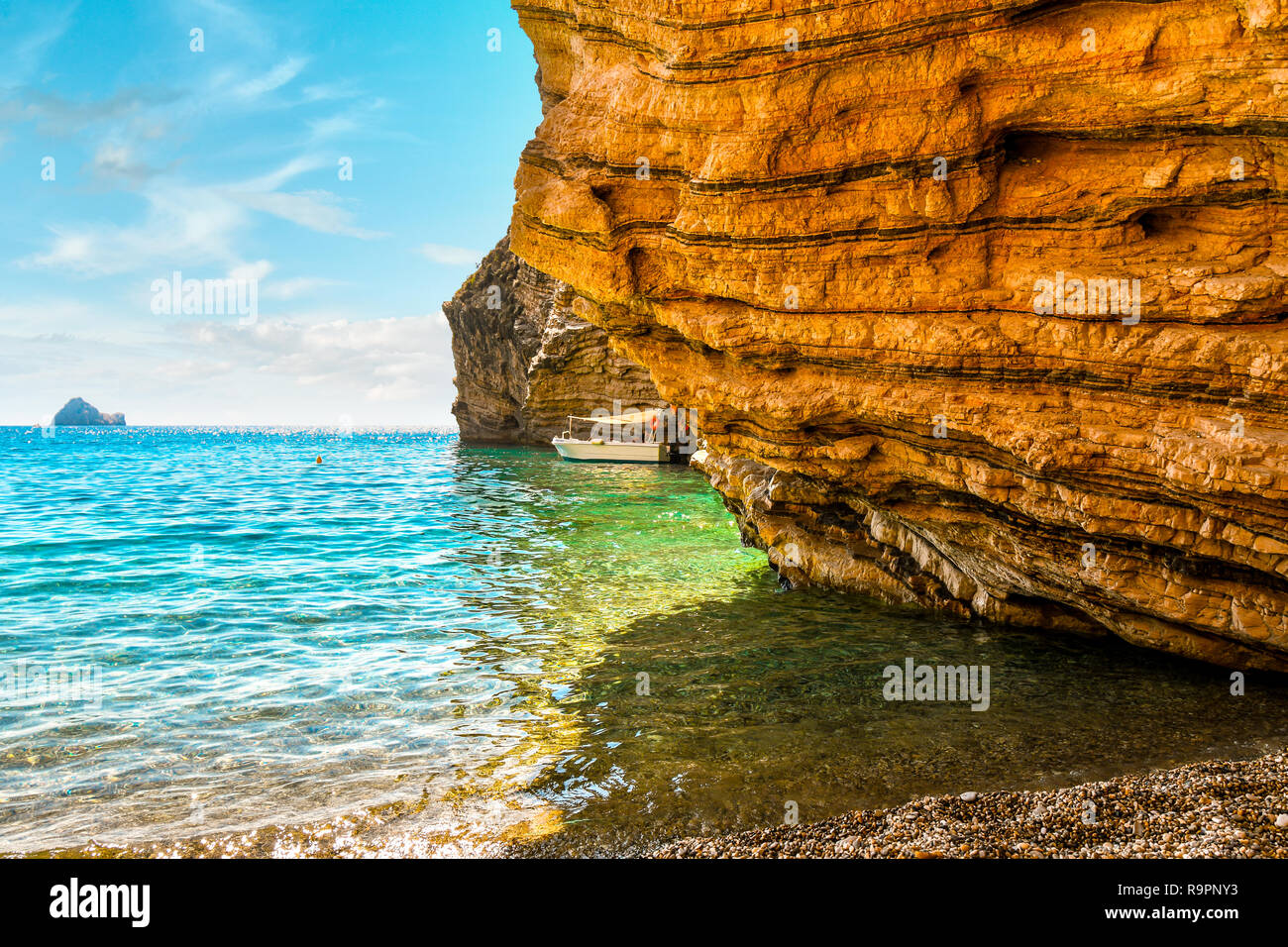A small boat docks against a rocky cove at Chomi Beach, also known as Paradise Beach, on a sunny summer day on the Greek island of Corfu, Greece. Stock Photo