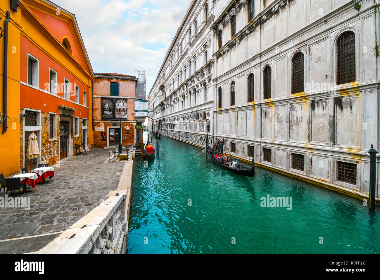 A Venetian gondolier with a family of tourists in his gondola, steers past a small square near the Bridge of Sighs in Venice, Italy Stock Photo