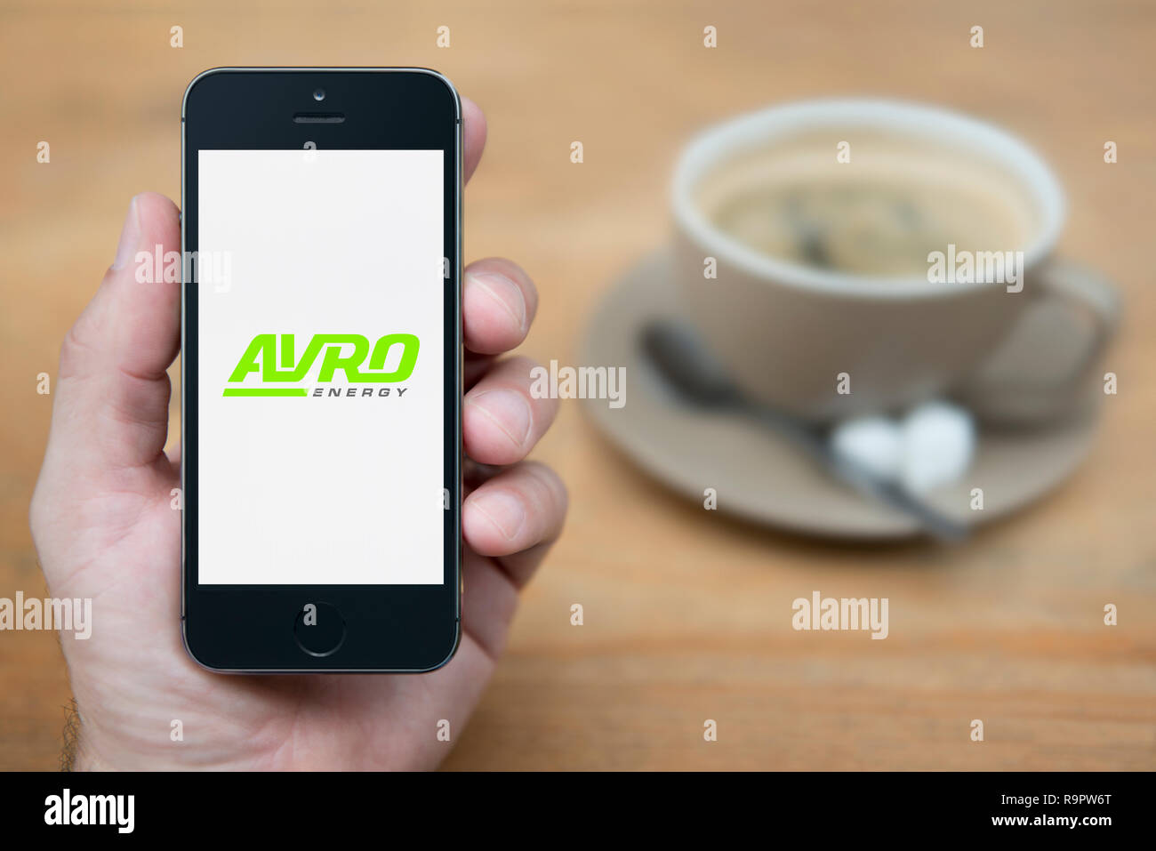 A man looks at his iPhone which displays the Avro Energy logo (Editorial use only). Stock Photo