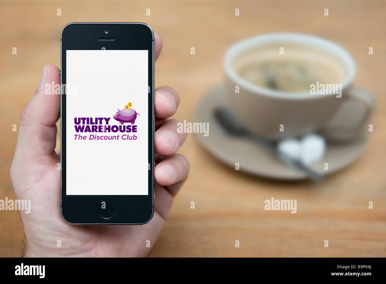A man looks at his iPhone which displays the Utility Warehouse logo (Editorial use only). Stock Photo