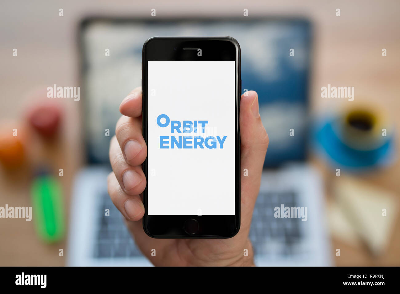 A man looks at his iPhone which displays the Orbit Energy logo (Editorial use only). Stock Photo