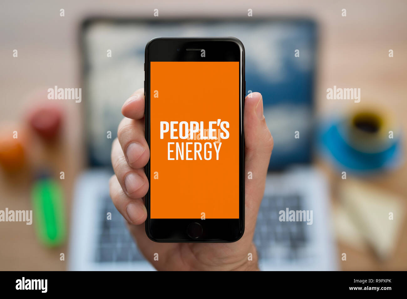 A man looks at his iPhone which displays the People's Energy logo (Editorial use only). Stock Photo