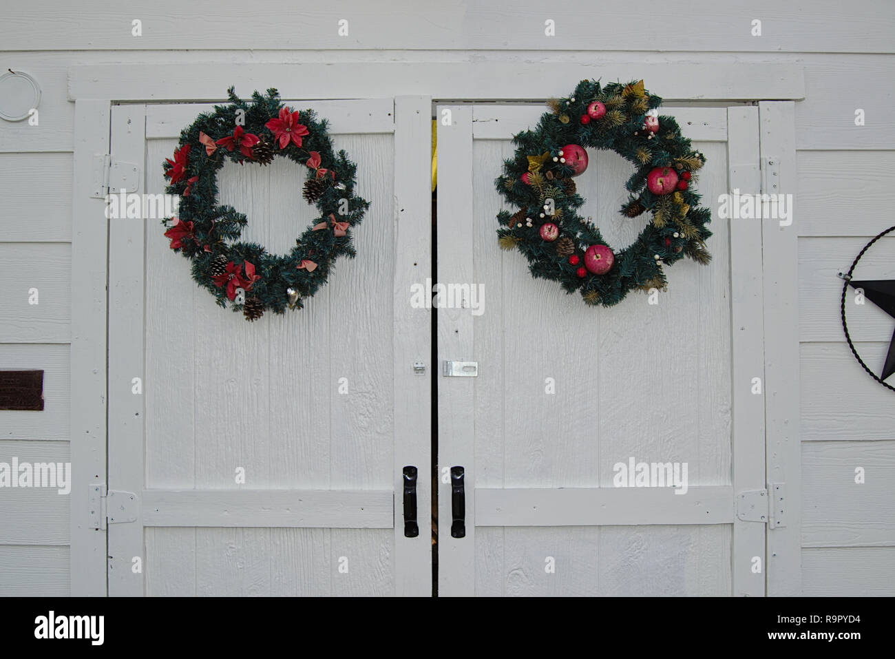 Two Wreaths Hanging On Double Doors Of White Building Stock