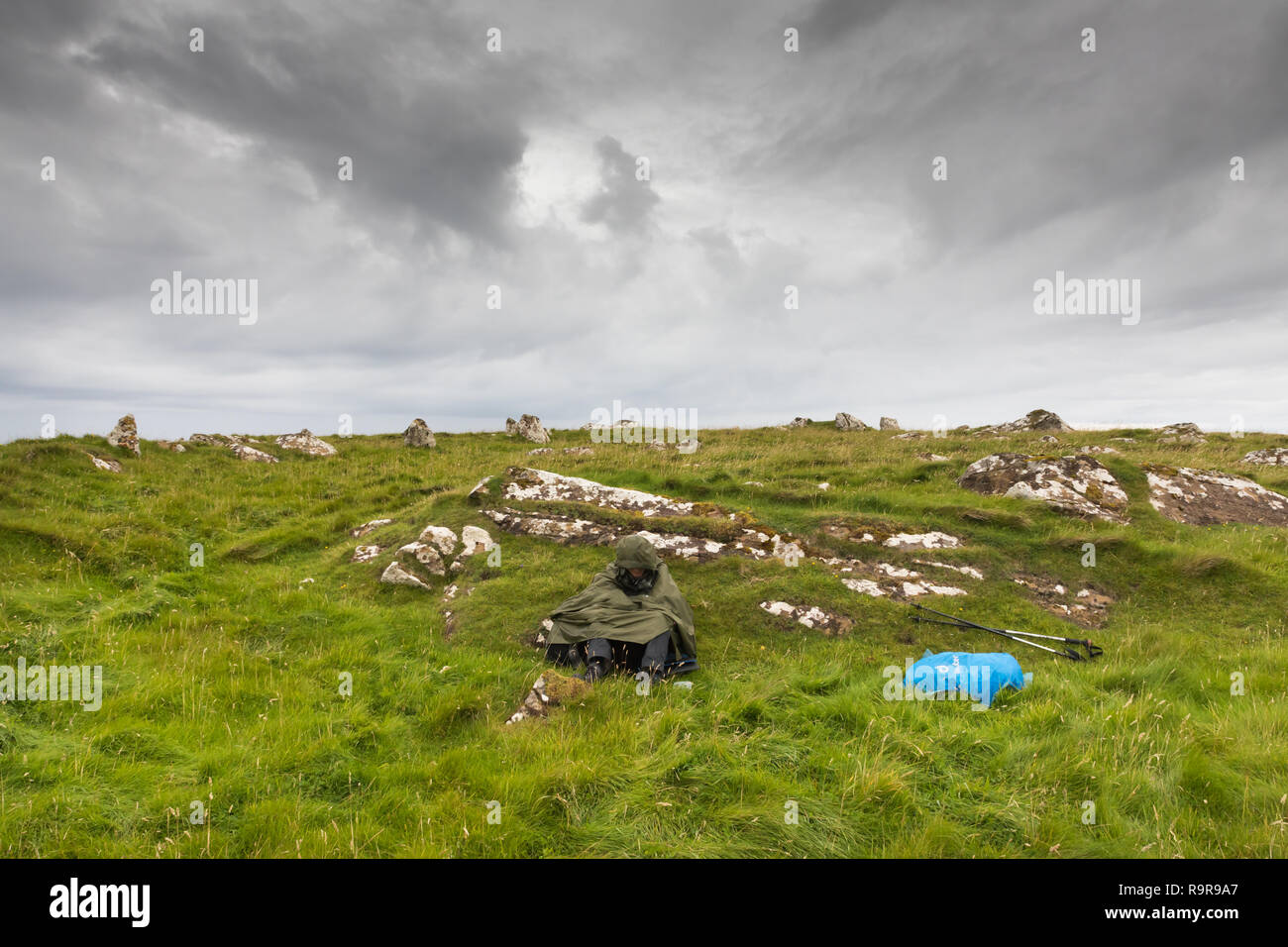 Person seeking protection against the rain, sitting on the grass. Fetlar, Shetland Islands. Stock Photo