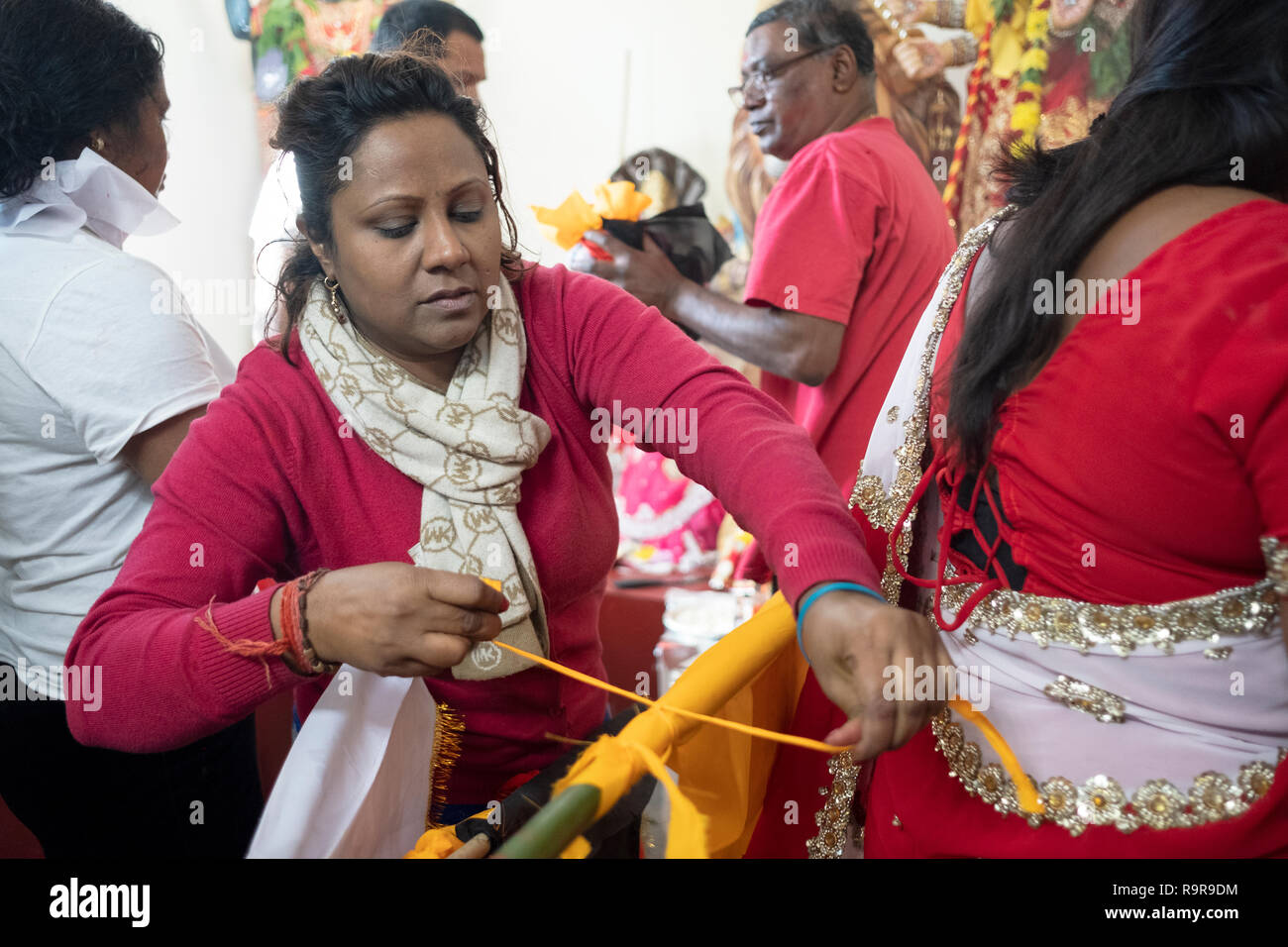 A devout Hindu woman ties a victory flag to a bamboo pole at a Shakti Temple in Jamaica, Queens, New York City. Stock Photo