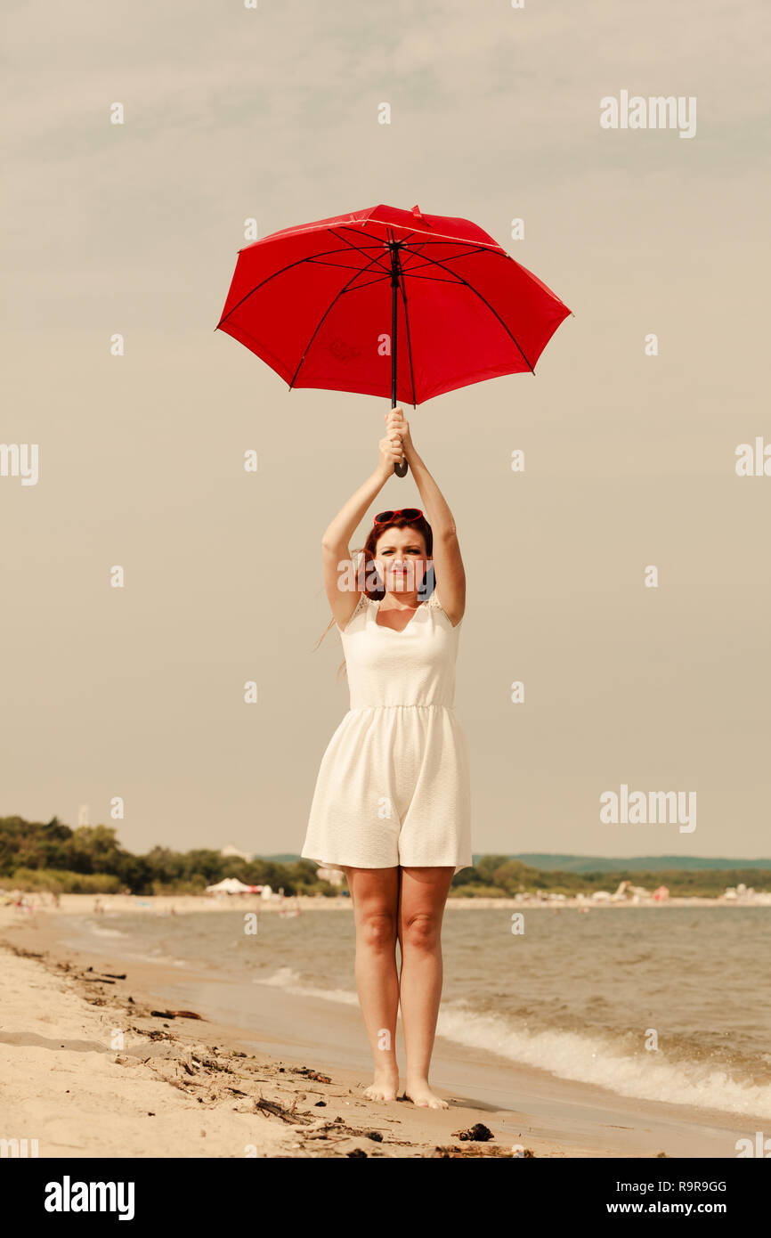 Redhead woman wearing gauzy white dress walking on beach jumping flying  while holding red umbrella Stock Photo - Alamy