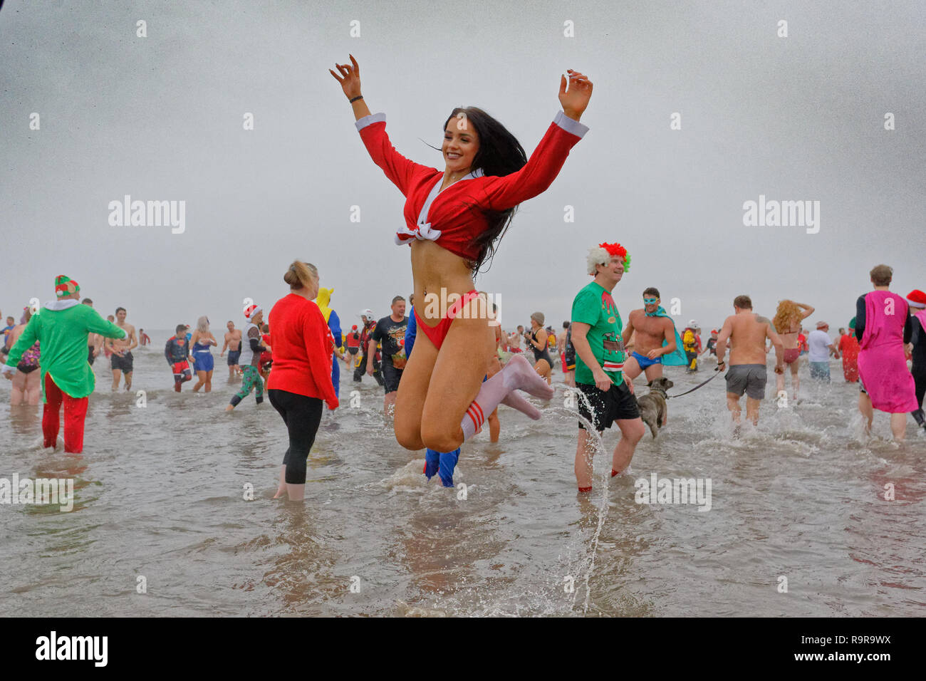 Pictured: A young woman in a Santa outfit jumps in the sea. Tuesday 25 December 2018 Re: Hundreds of people take part in this year's Porthcawl Christm Stock Photo