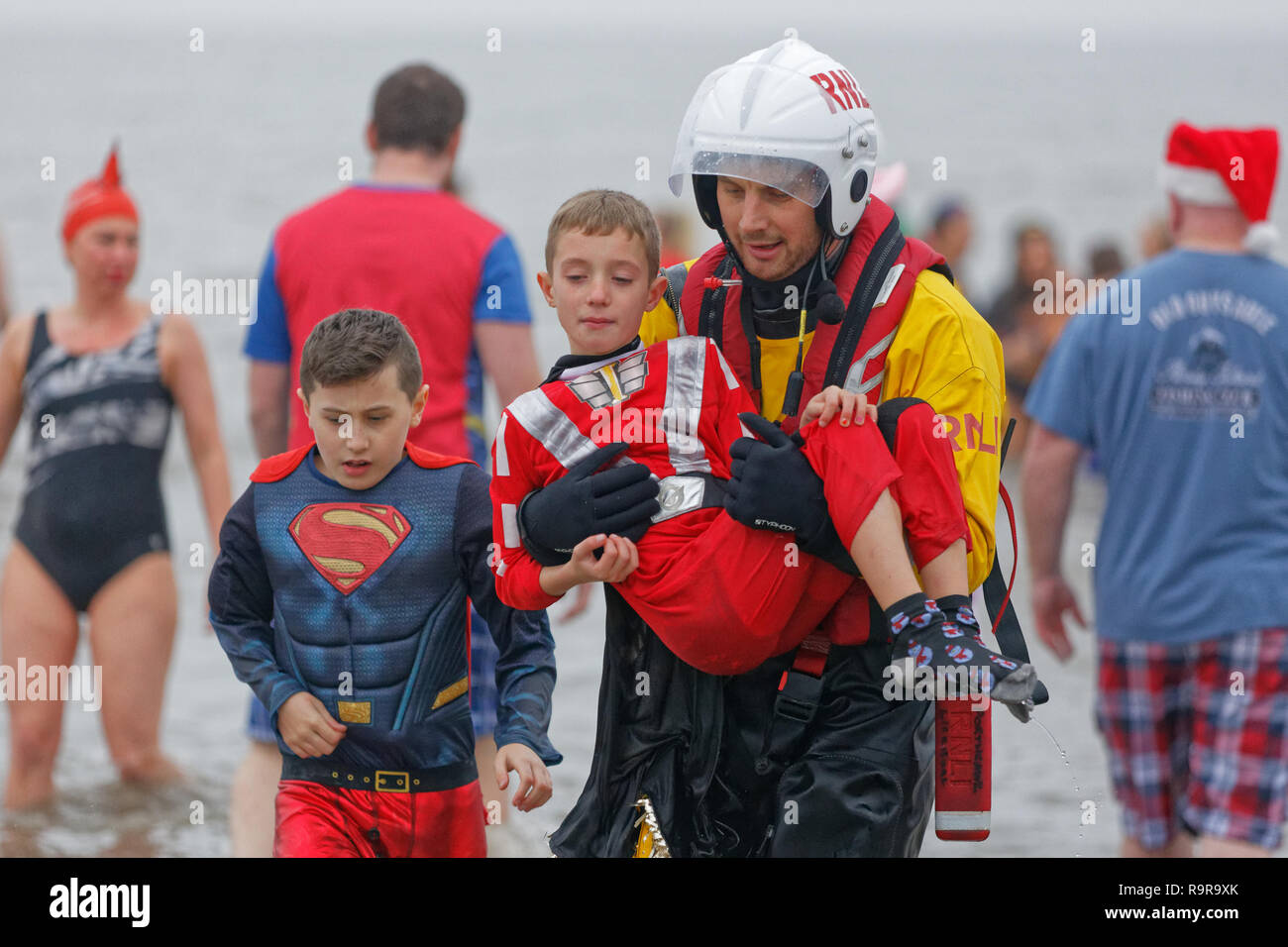 Pictured: A young boy is carried back to safety by an RNLI rescuer. Tuesday 25 December 2018 Re: Hundreds of people take part in this year's Porthcawl Stock Photo