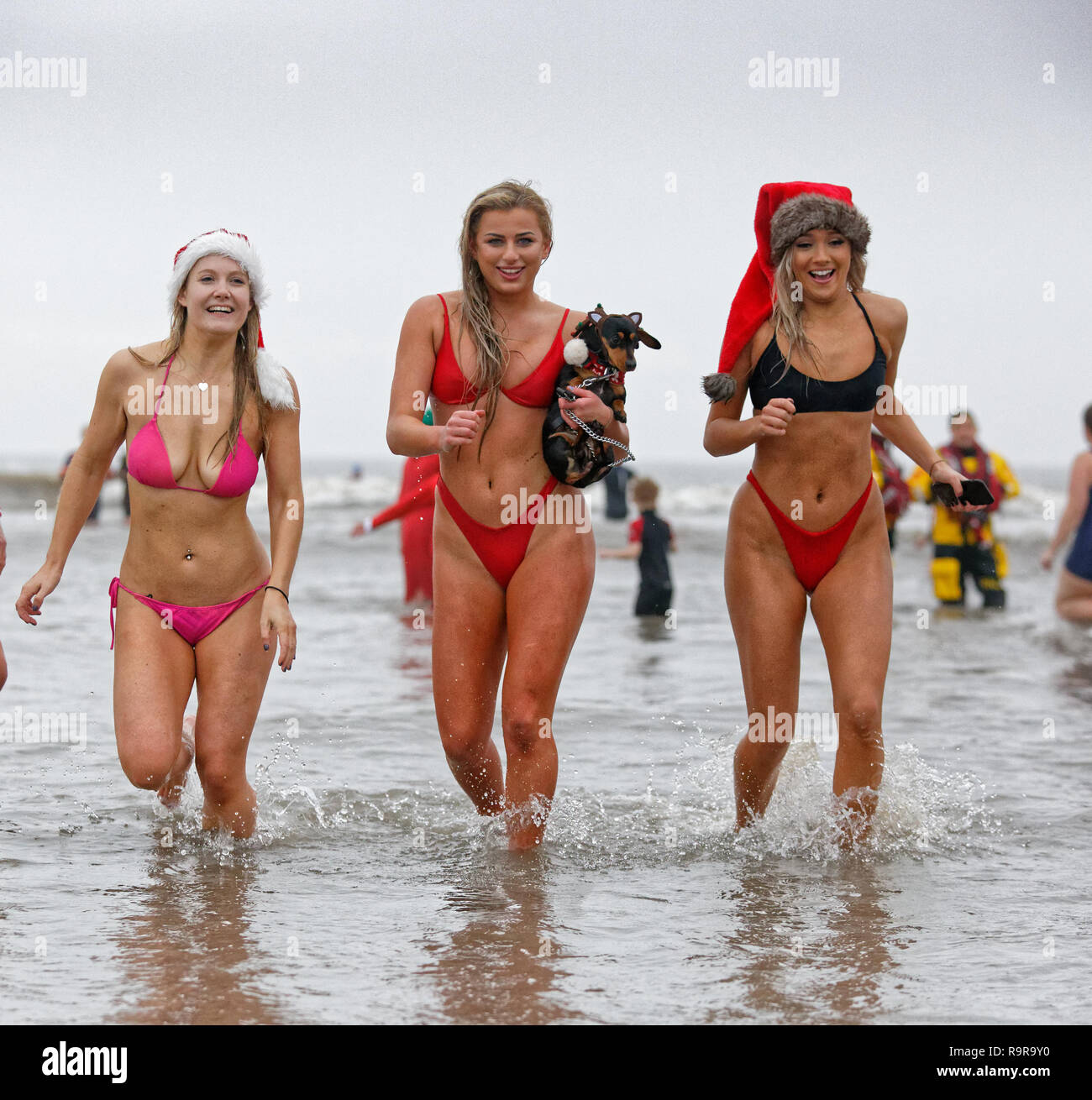Pictured: Three young women in bikinis and Santa hats run in the sea.  Tuesday 25 December 2018 Re: Hundreds of people take part in this year's Porthc Stock Photo